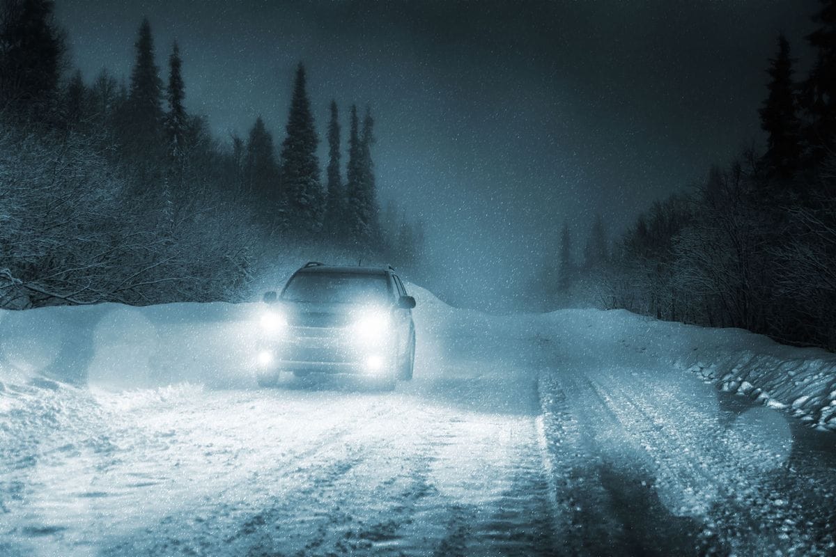 Auto mit eingeschaltetem Licht nachts auf einer verschneiten Waldstraße